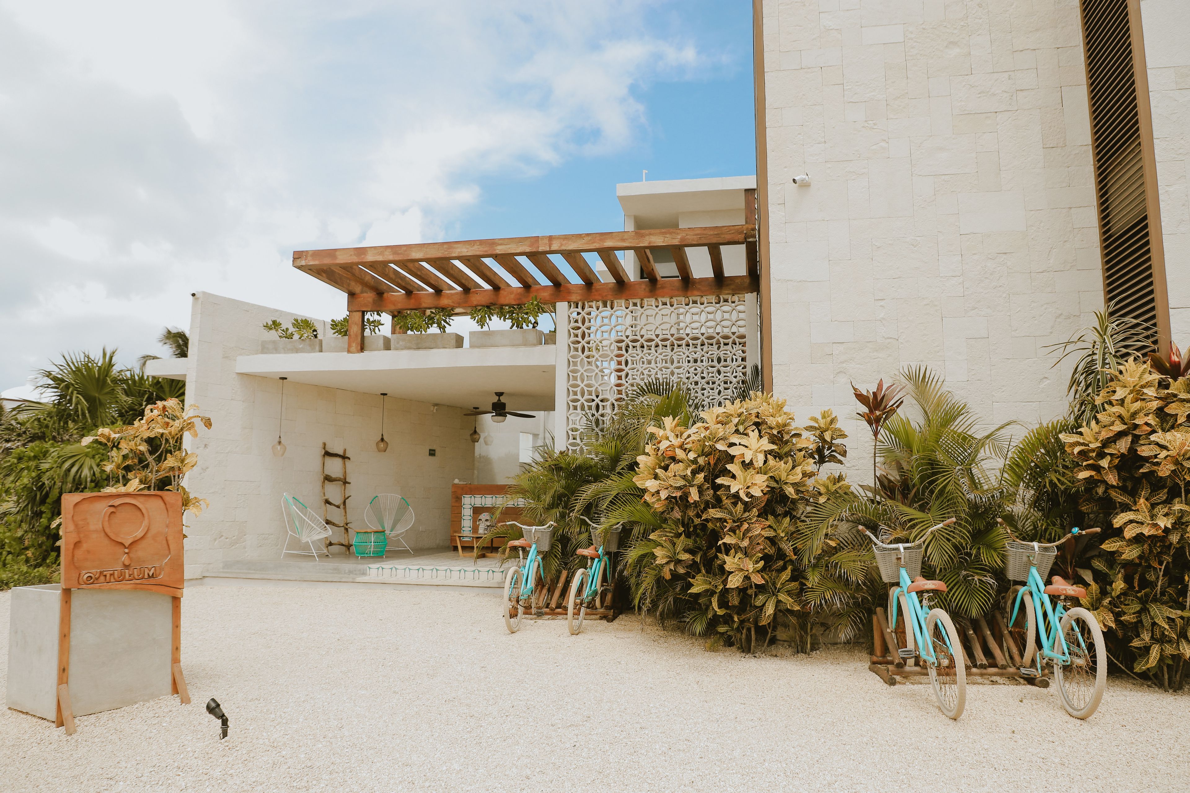 A modern building with a white facade, a wooden pergola, and a gravel driveway.