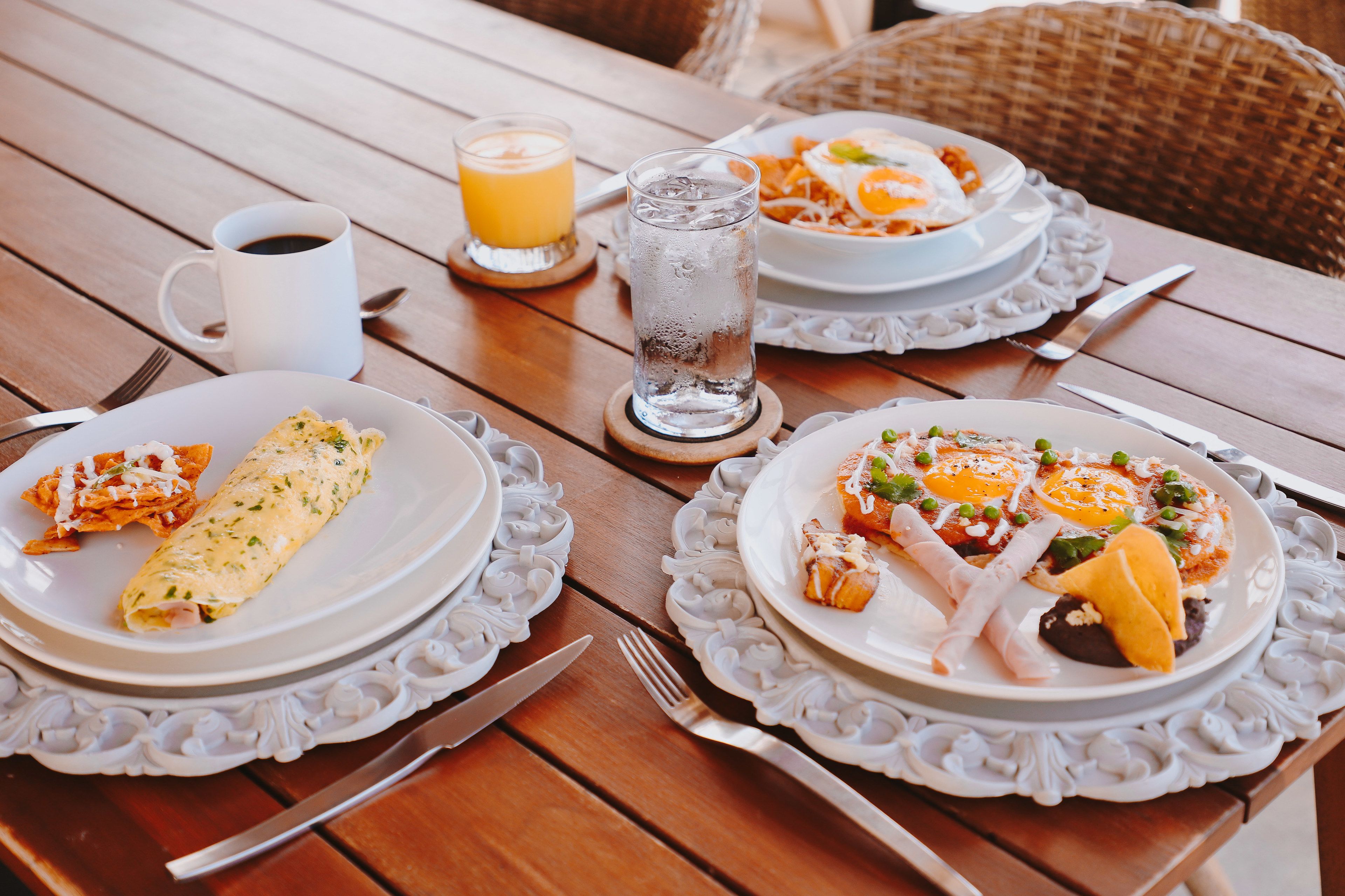A wooden dining table with plates of food, a glass of water, and a cup of coffee.