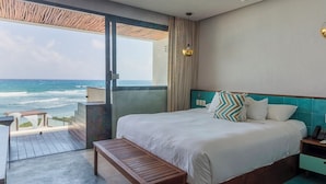 Quarto de hotel com uma cama grande, um banco de madeira, vista para o oceano e uma varanda com deck de madeira.