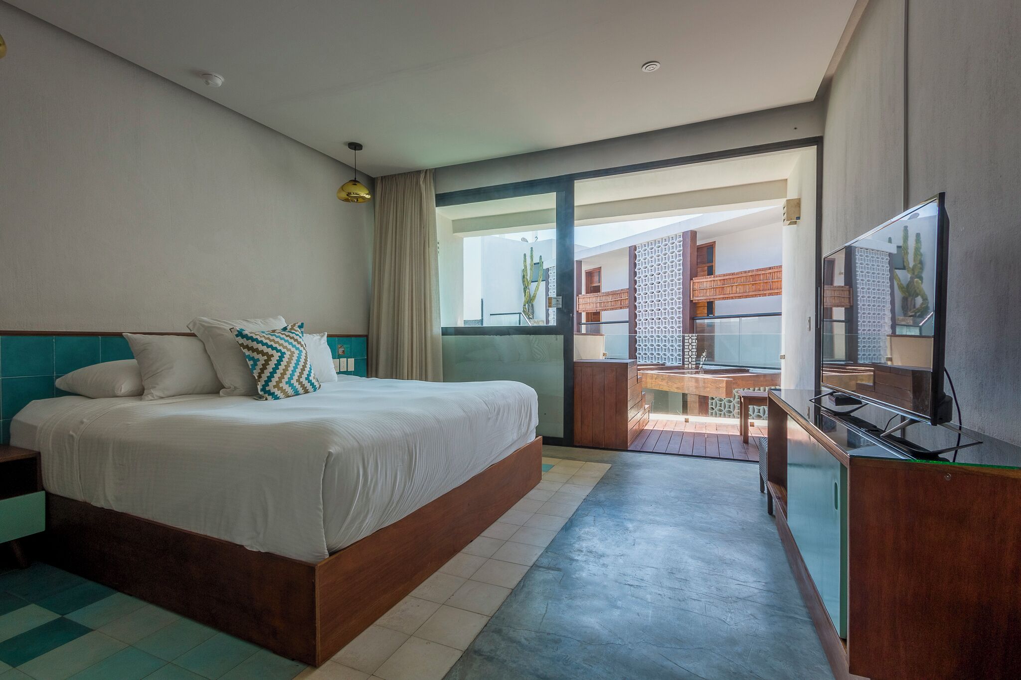 A hotel room with a bed, a TV, a desk, and a view of the outdoor area.