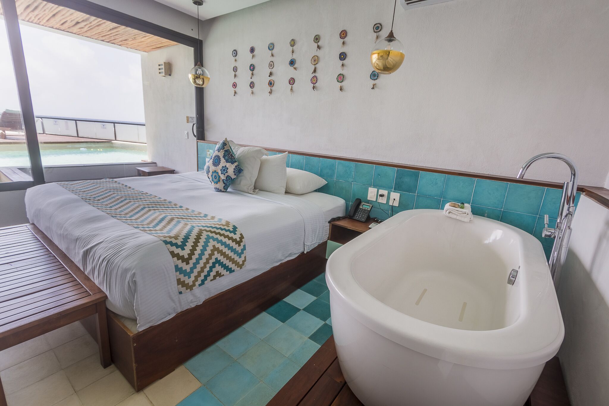 A bedroom with a large bed, a bedside table, a wall-mounted phone, a wall-mounted light fixture, a large bathtub, and a view of an outdoor swimming pool.