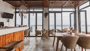 Um restaurante à beira-mar com balcão de madeira, mobiliário de vime e amplas janelas com vista para o mar.