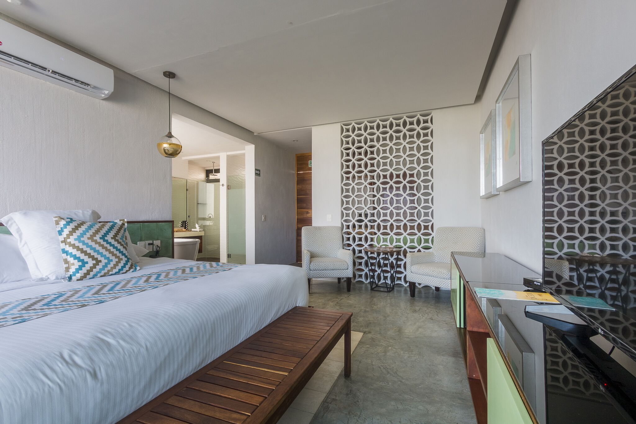 Habitación de hotel con cama, un banco, un escritorio y un papel tapiz estampado.