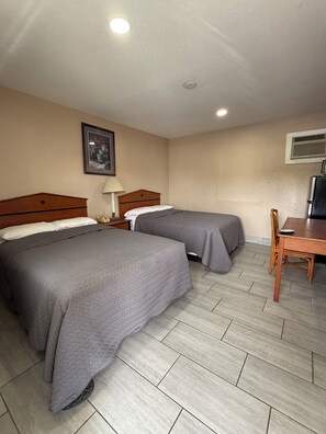 A hotel room with two beds, a desk, a chair, a lamp, and a picture on the wall.