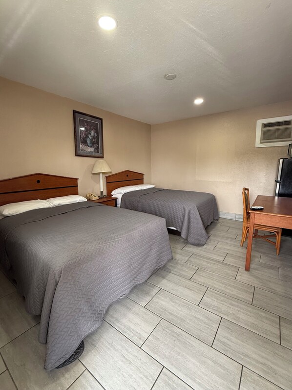 A hotel room with two beds, a desk, a chair, a lamp, and a picture on the wall.