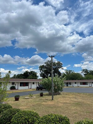 A motel with two-story buildings, a parking lot, and a grassy area with potted plants.