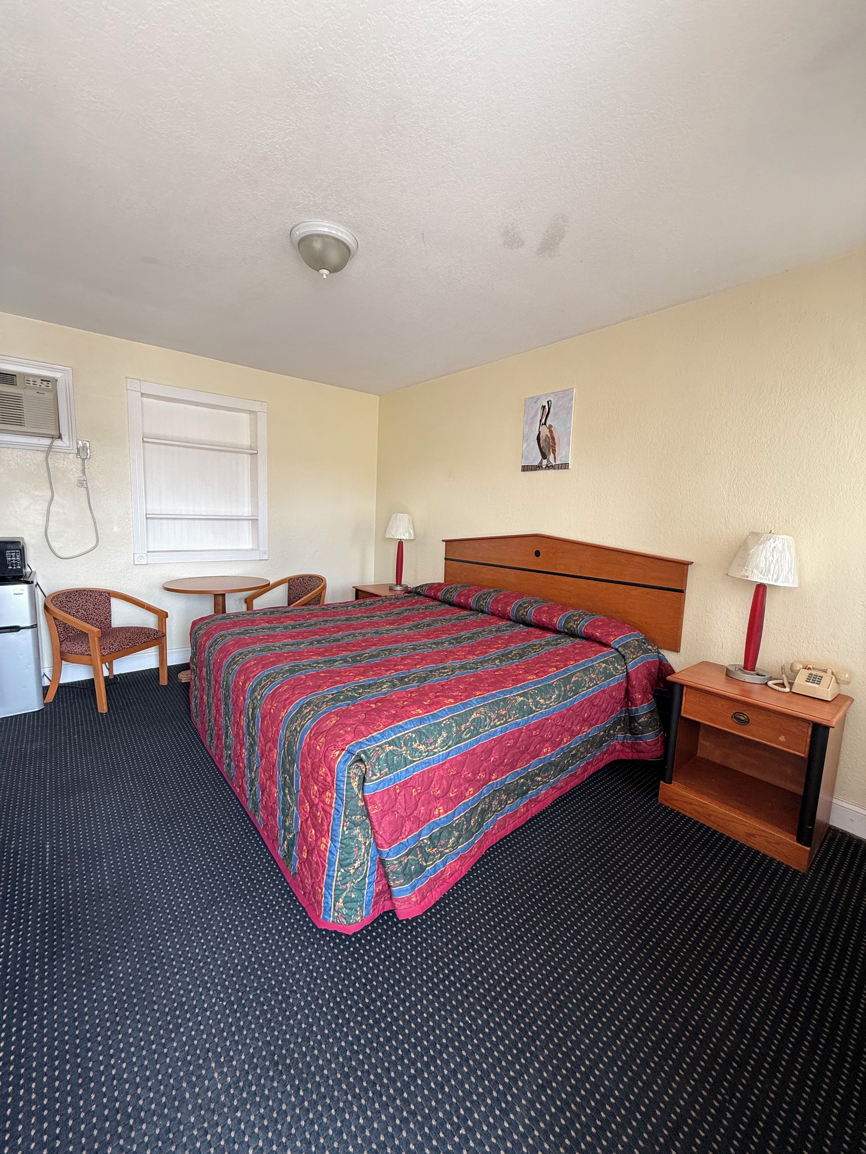 A hotel room with a bed, a desk, a chair, a lamp, and a telephone.