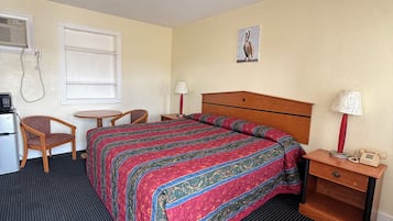 A hotel room with a bed, a desk, a chair, a lamp, and a telephone.