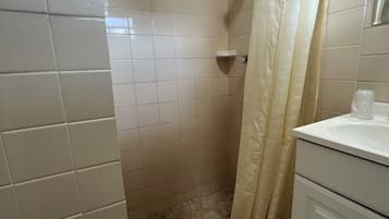 A bathroom with white tiled walls, a shower with a hexagonal floor pattern, a white sink, and a towel hanging on the wall.
