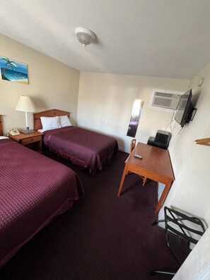 A hotel room with two beds, a desk, a chair, a TV, and a telephone.