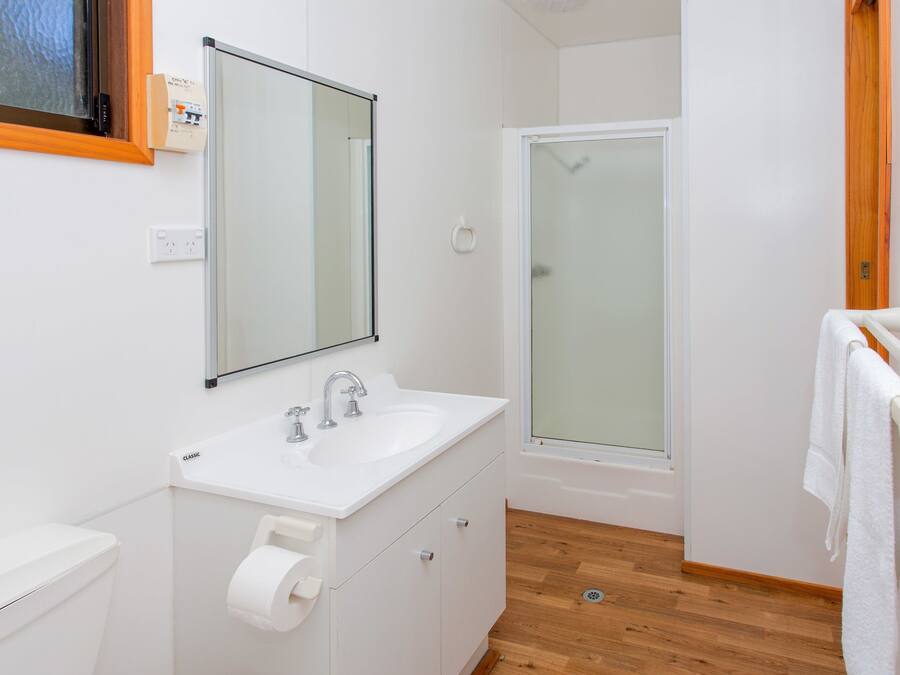 Un baño moderno con lavamanos, espejo y ducha blancos.