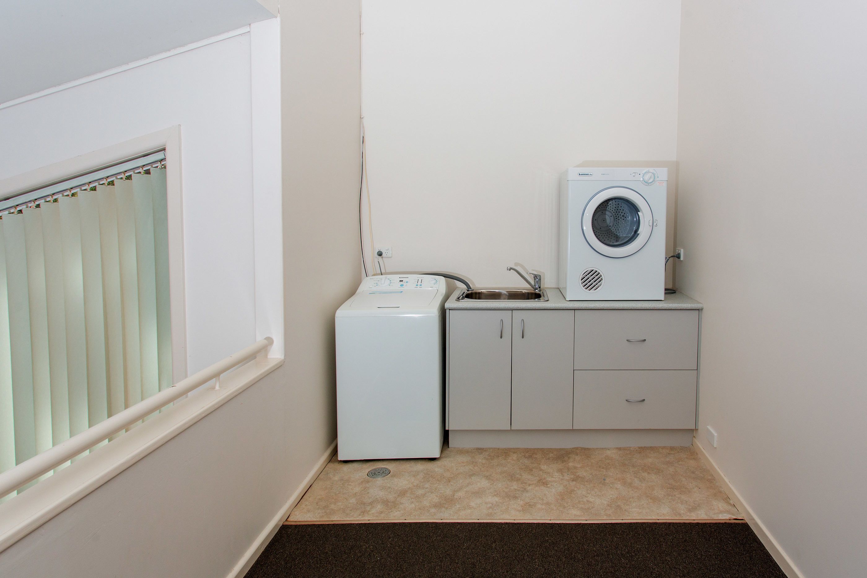 Un espace buanderie compact comprenant un lave-linge, un sèche-linge et un petit évier.