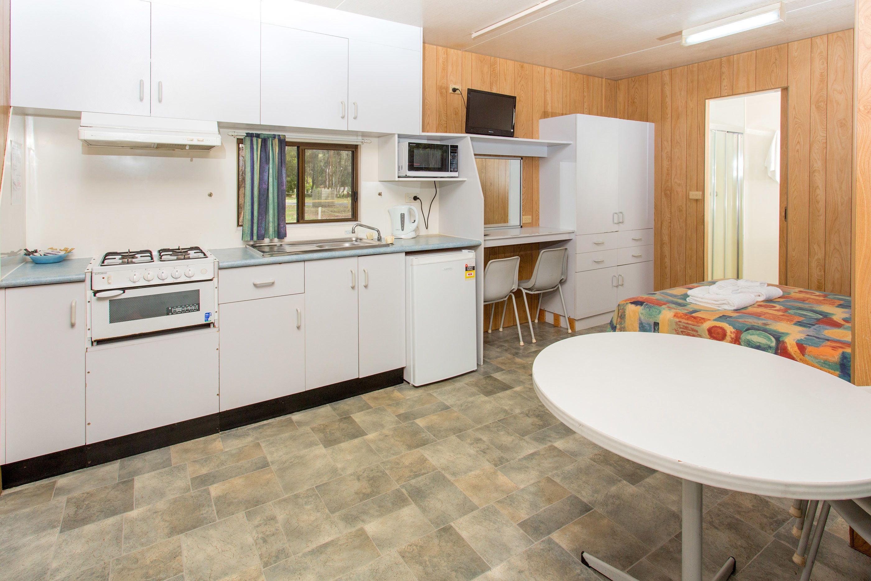 A compact kitchen with a gas stove, microwave, and a small sink. There's a dining table and a single chair.