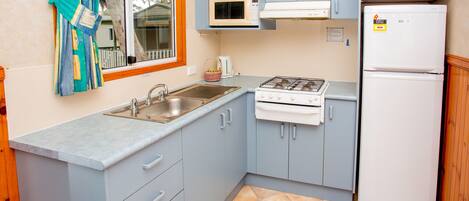 A compact kitchen with a sink, stove, microwave, and refrigerator.