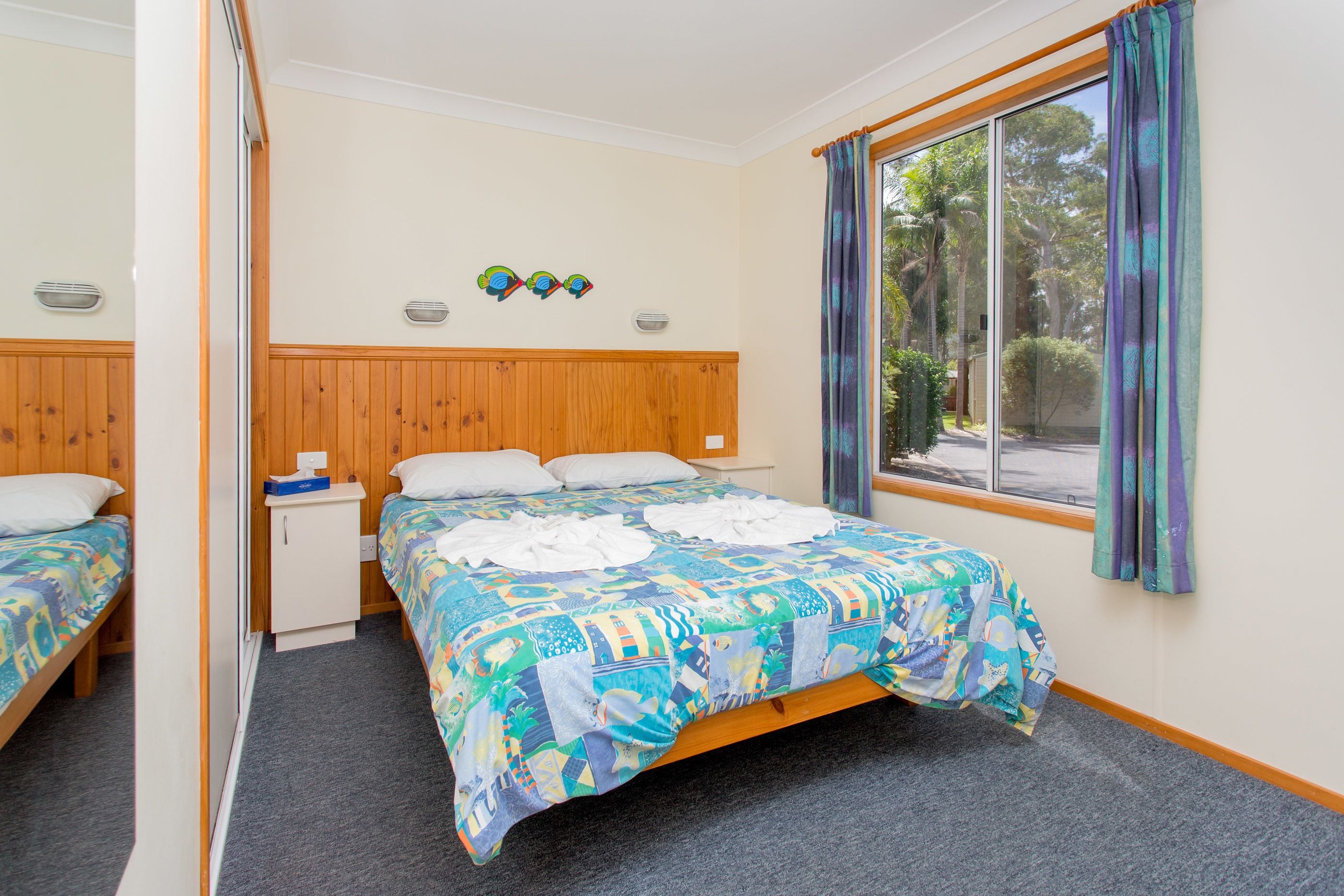 A hotel room with a bed, a small bedside table, a mirror, and a window with curtains.