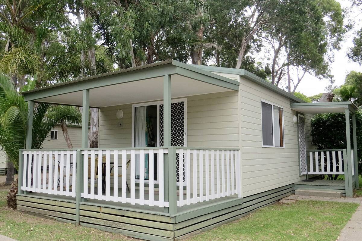 Een klein, gelijkvloers huis met een veranda en een omheind terras.