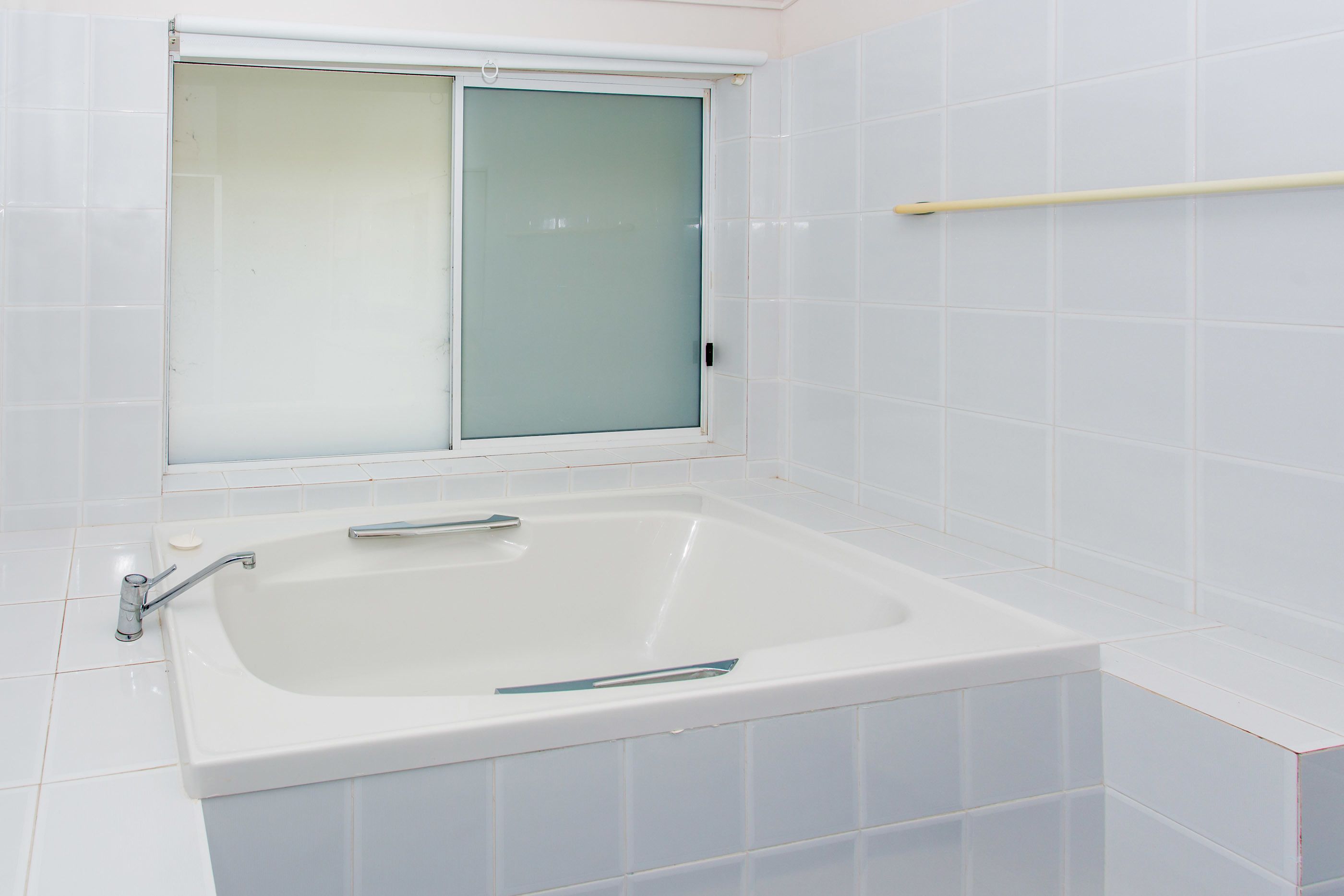Un baño con una bañera blanca, un ventanal con vidrio esmerilado y paredes cubiertas de azulejos blancos.
