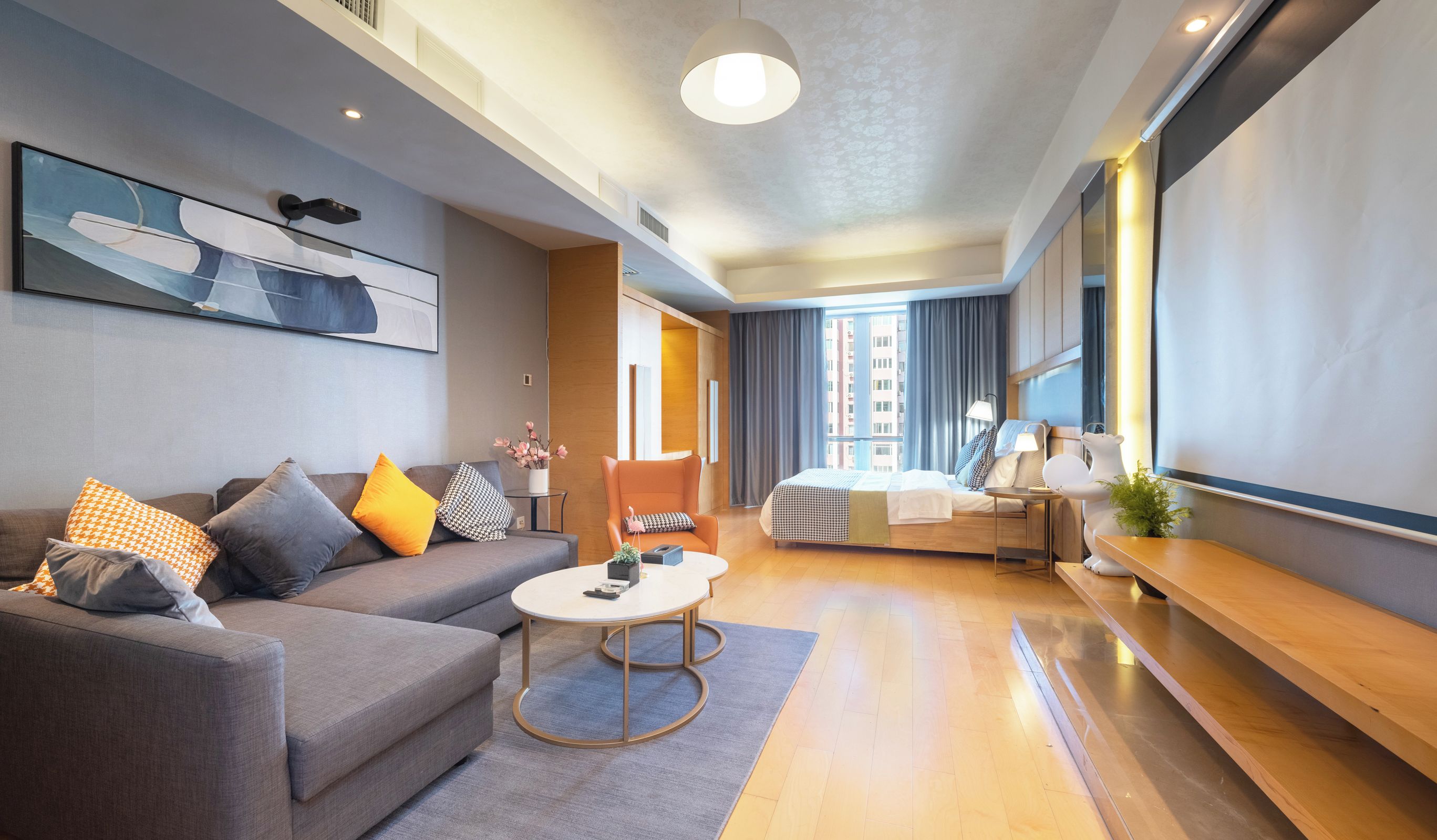 A modern hotel room with a sofa, armchair, round table, and a bed with a view of the city.
