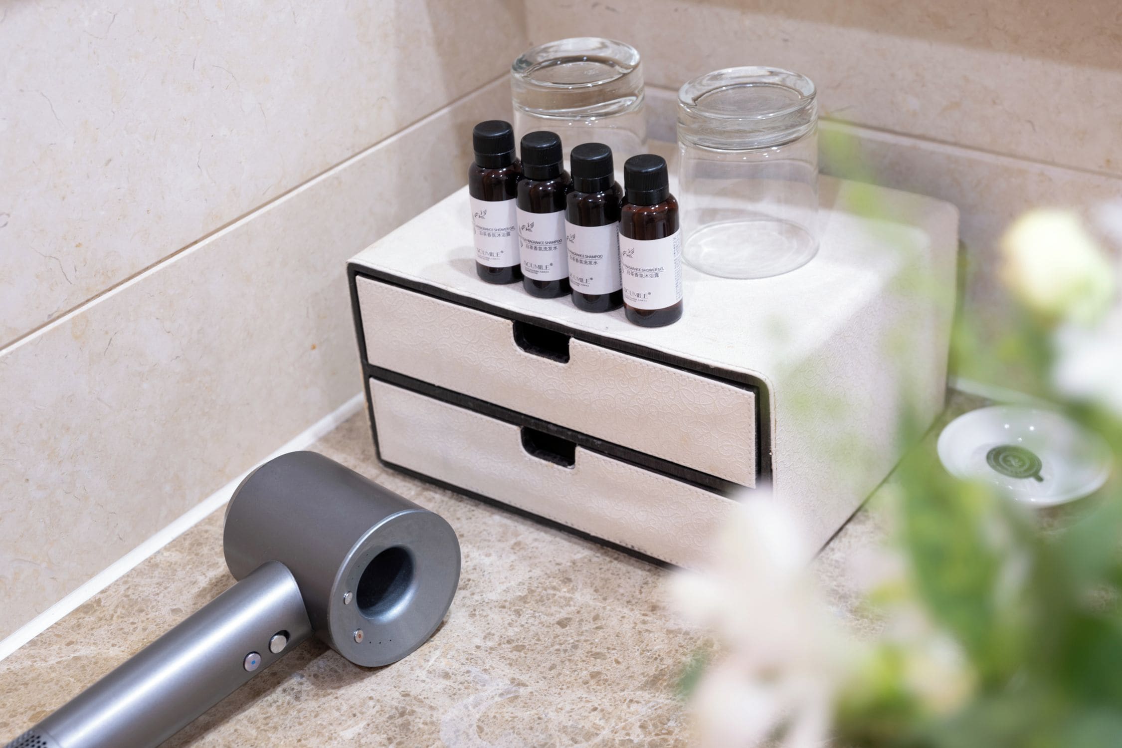 Un tocador de baño con un mueble de madera, un secador de pelo y tres botellas de gel de ducha.