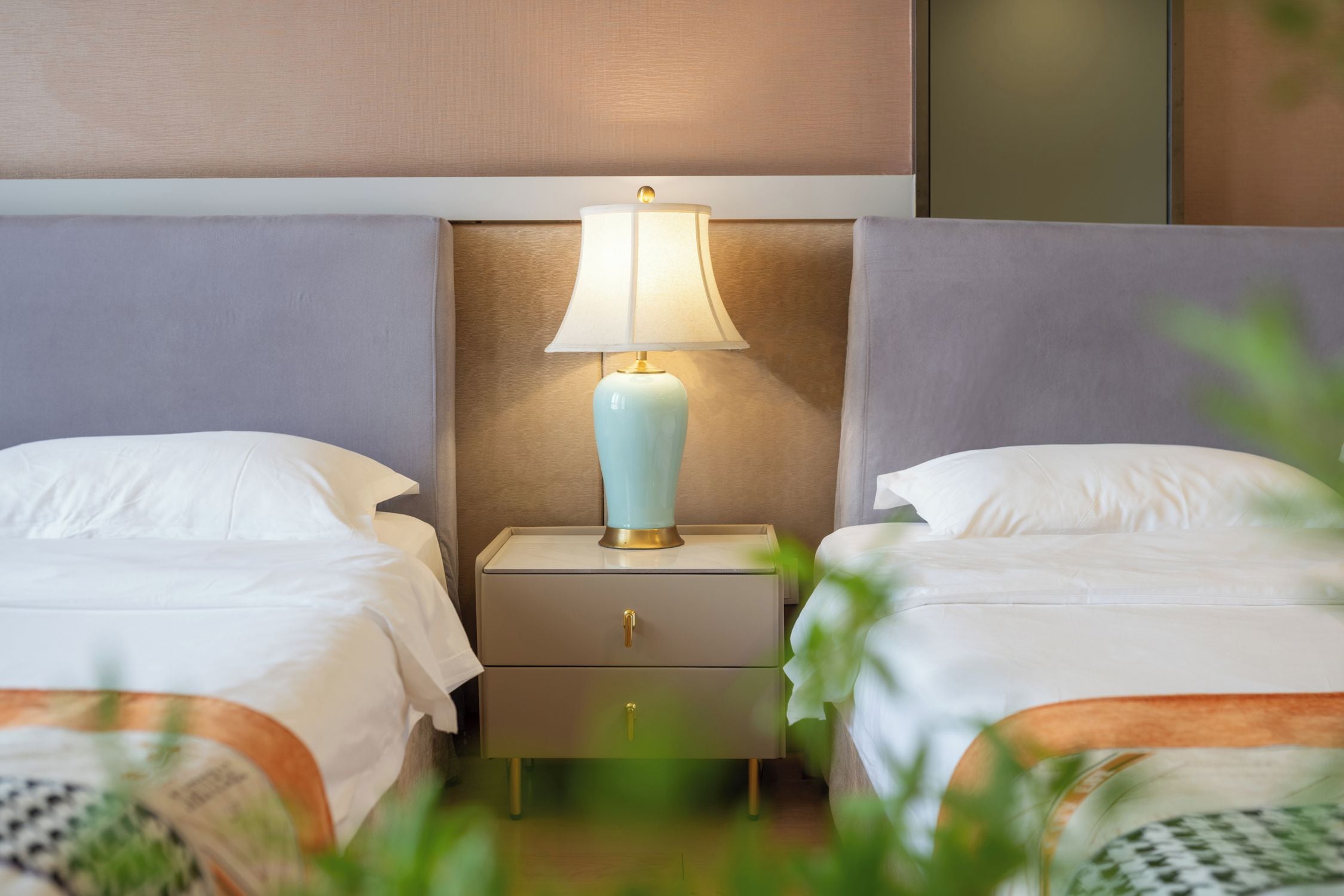 Ein Hotelzimmer mit zwei Betten, einem Nachttisch mit Lampe und einer wandmontierten Vertäfelung.