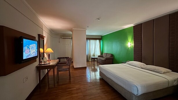 A hotel room with a bed, a desk with a lamp, a television, and a green accent wall. - Hotel Mega Cikini (Jakarta)