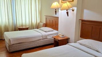 A hotel room with two beds, a small table, a lamp, and a painting on the wall.