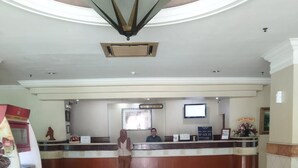 A hotel reception area with a marble floor, a reception desk, a television, and a vending machine. - Hotel Mega Cikini (Jakarta)