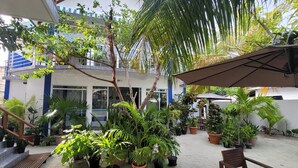 A courtyard with potted plants, a wooden bench, and a large umbrella. - Palm Residence (Rasdhoo)