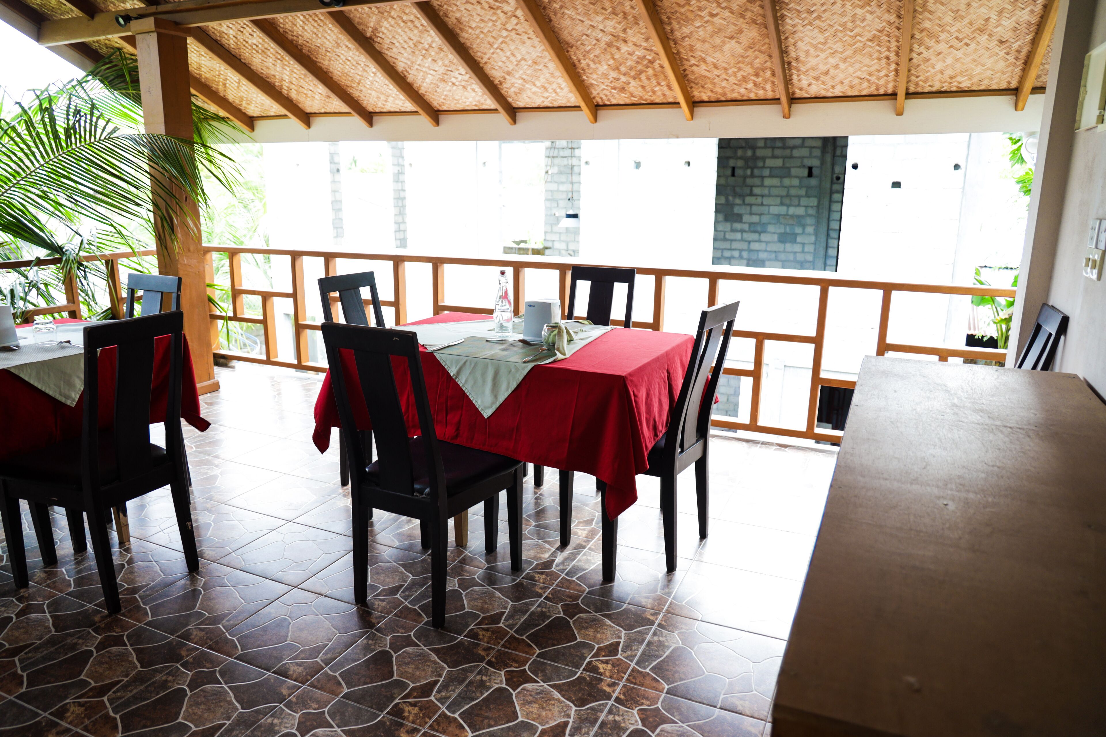 Een restaurant met terras, rode tafelkleden en een rieten dak.
