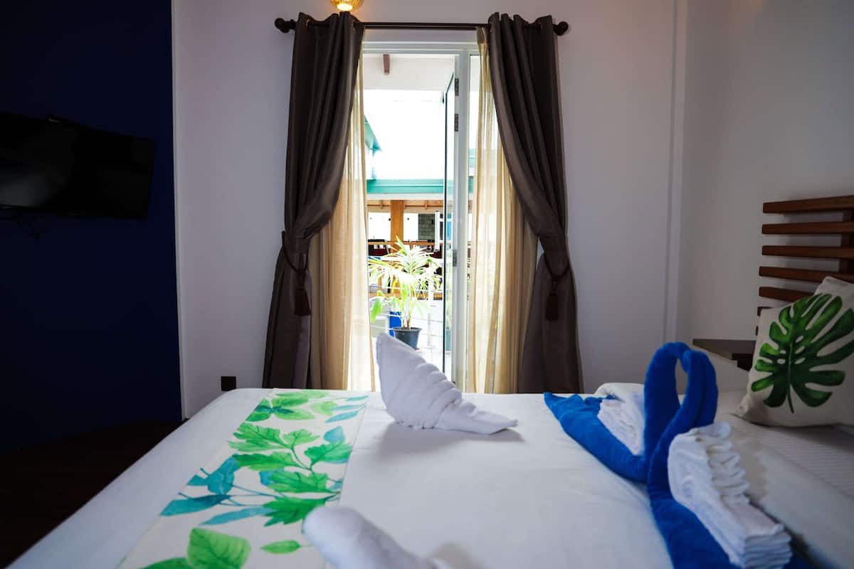 A hotel room with a bed, curtains, a TV mounted on the wall, and a view of the outside.