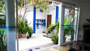 A modern interior with a glass door leading to a courtyard with potted plants and a wooden bench. - Palm Residence (Rasdhoo)