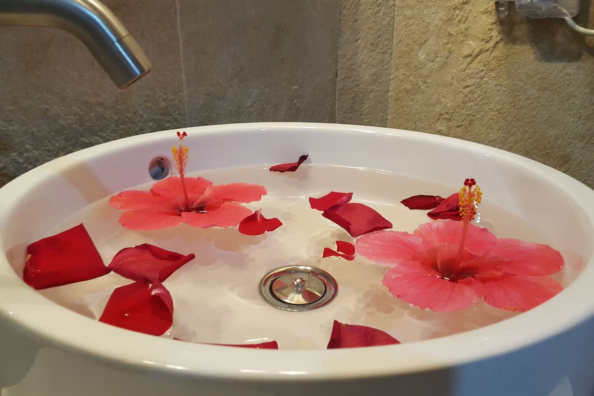 A white sink with red flower petals and yellow flowers floating in water.
