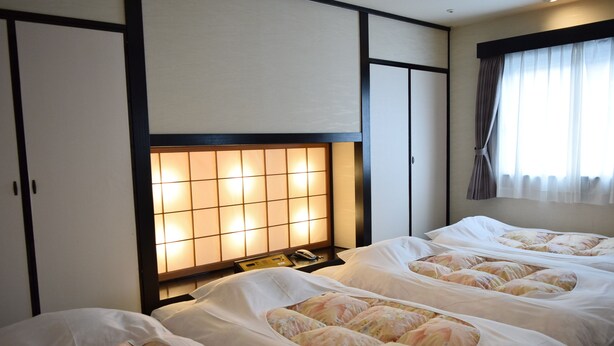 A hotel room with four beds, a traditional Japanese-style headboard, and a large window with curtains. - Asakusa Central Hotel (Tokyo)
