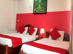 A hotel room with two beds, red walls, a painting of a tree-lined path, and a bedside lamp.