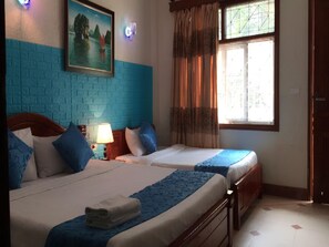 A hotel room with two beds, a painting on the wall, a window with curtains, and a nightstand with a lamp.
