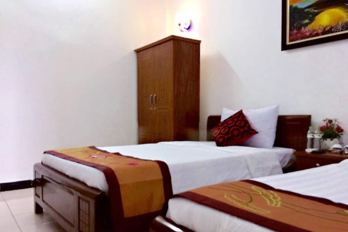 A hotel room with two single beds, a wooden wardrobe, a nightstand with a lamp, and a painting on the wall.