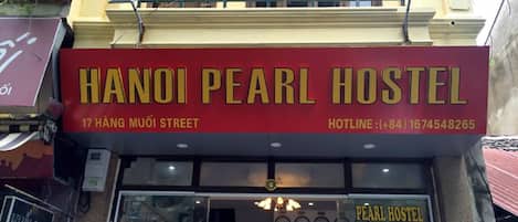 Exterior del Hanoi Pearl Hostel, con un letrero rojo, dirección y número de teléfono de contacto.