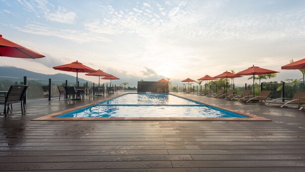 A swimming pool with red umbrellas, lounge chairs, and a wooden deck. - The Smith House (Langkawi)