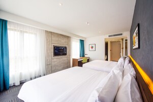 Habitación de hotel con dos camas, un escritorio, un televisor y una puerta que da a otra habitación.
