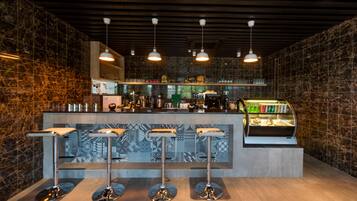 A modern bar area with a marble backsplash, three bar stools, overhead pendant lighting, and a refrigerated display case.
