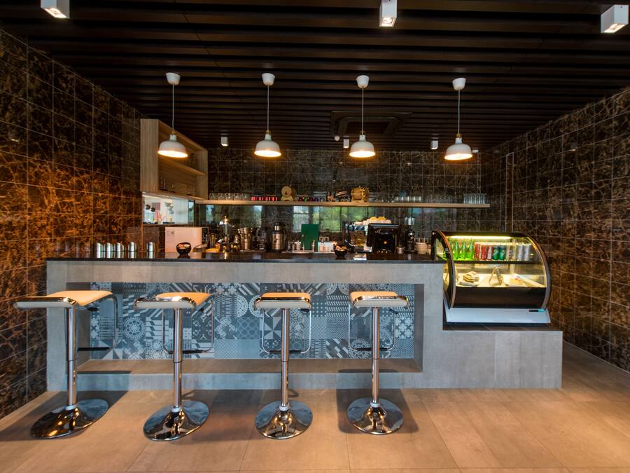 A modern bar area with a marble backsplash, three bar stools, overhead pendant lighting, and a refrigerated display case.