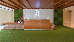 A reception area with a wooden reception desk, green artificial grass, and a reception sign. - The Smith House (Langkawi)