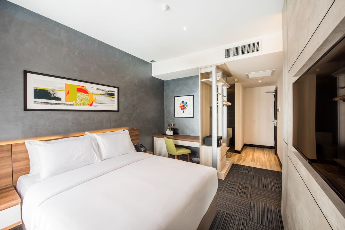 A hotel room with a large bed, a desk, and a chair. There is a framed picture on the wall and a window with a view.