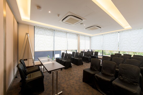 Un salón de conferencias con hileras de sillas, una mesa y ventanas amplias con vistas.