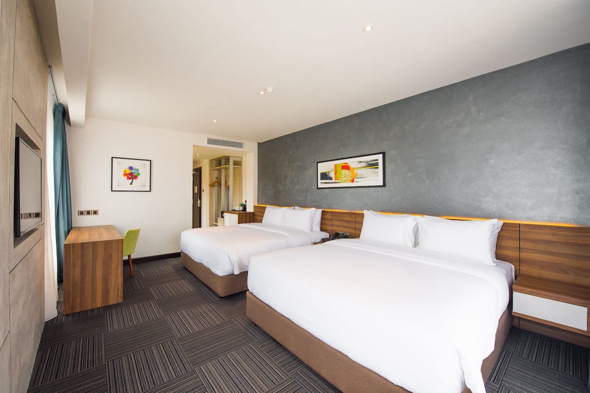 A hotel room with two beds, a wooden desk, and a chair.
