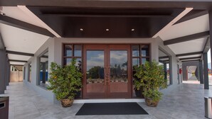 A modern building entrance with a glass door, two potted orange trees, and a black mat. - The Smith House (Langkawi)