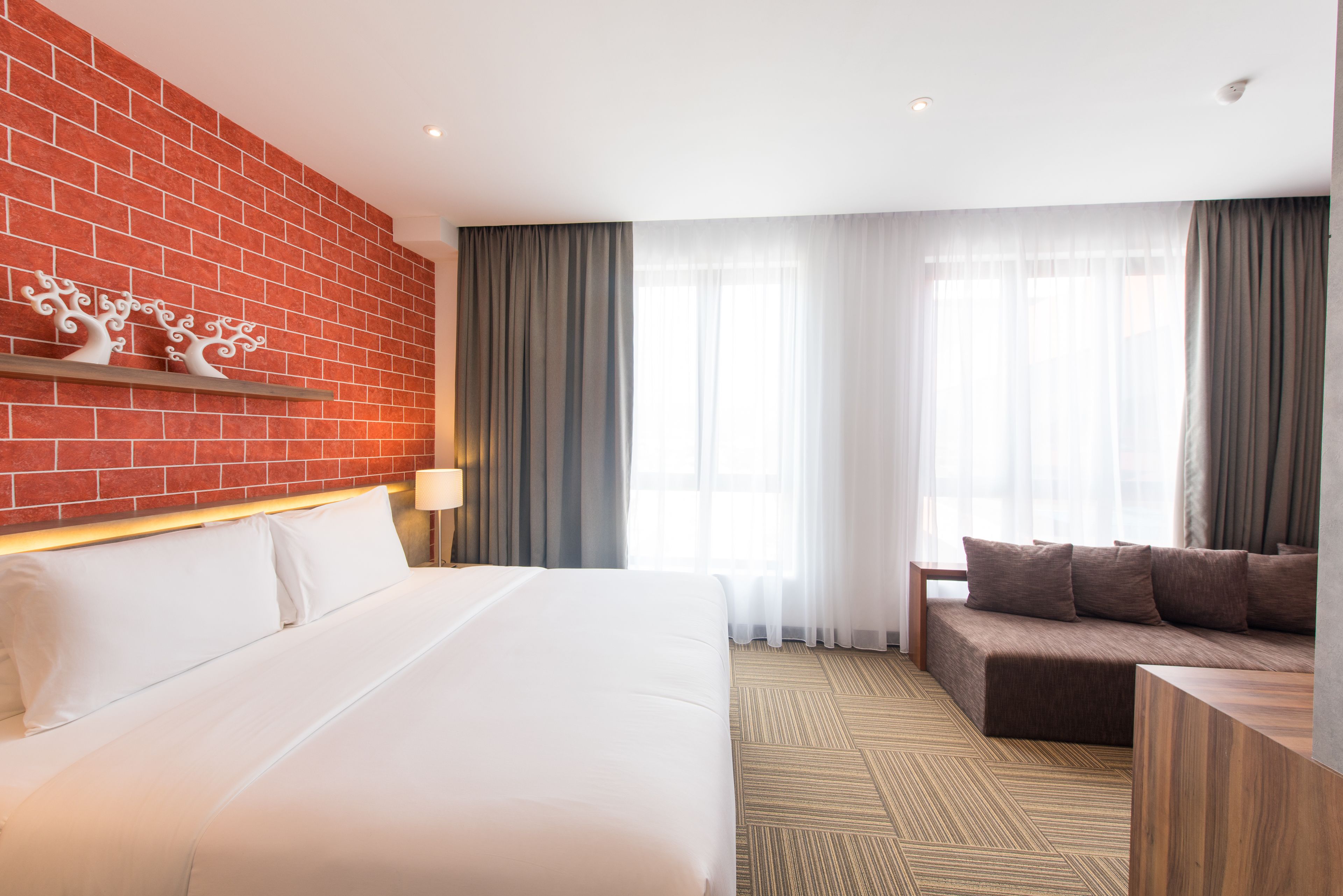 A hotel room with a large bed, a sofa, a brick wall, and a window with curtains.