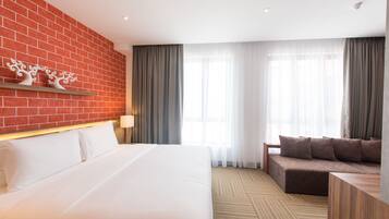 Habitación de hotel con una cama grande, un sofá, una pared de ladrillo y una ventana con cortinas.