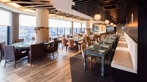 A modern restaurant with high ceilings, wooden beams, and large windows offering city views. Tables are set with green placemats and white tablecloths. - The Smith House (Langkawi)