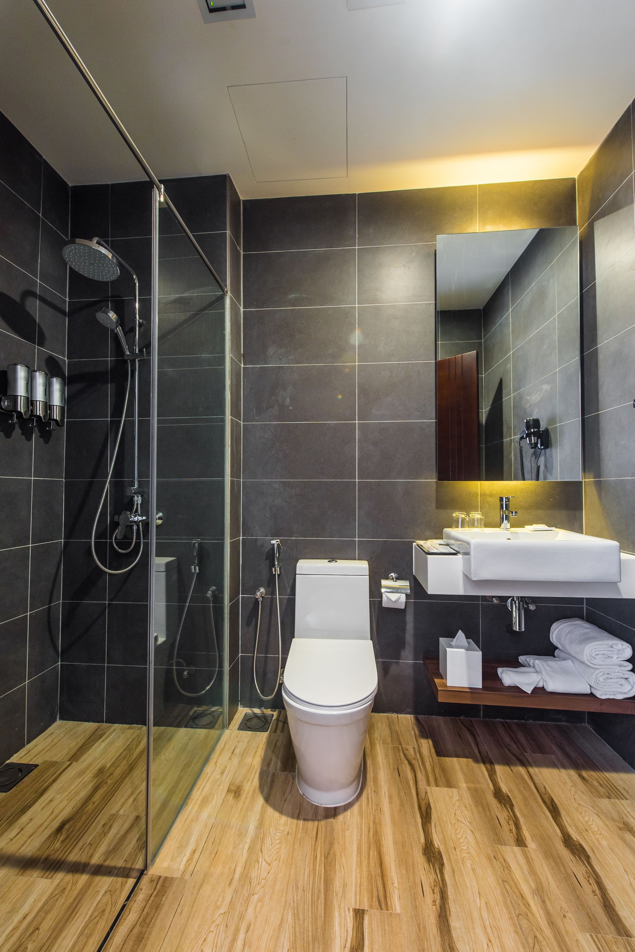 Une salle de bain moderne avec une douche à parois de verre, des toilettes blanches et un meuble-lavabo en bois doté d’un évier et d’un miroir.